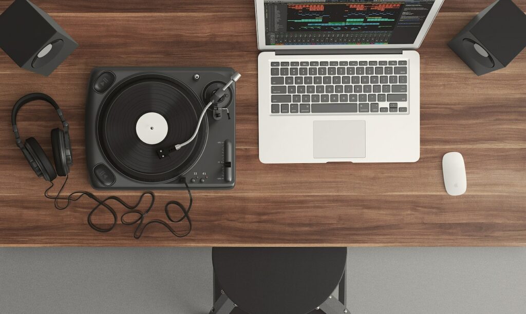 A laptop running an audio mixing program with a turntable, headphones, speakers, and a mouse beside it.