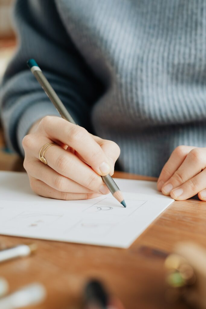 An artist sitting at their desk working on a drawing with a pencil.