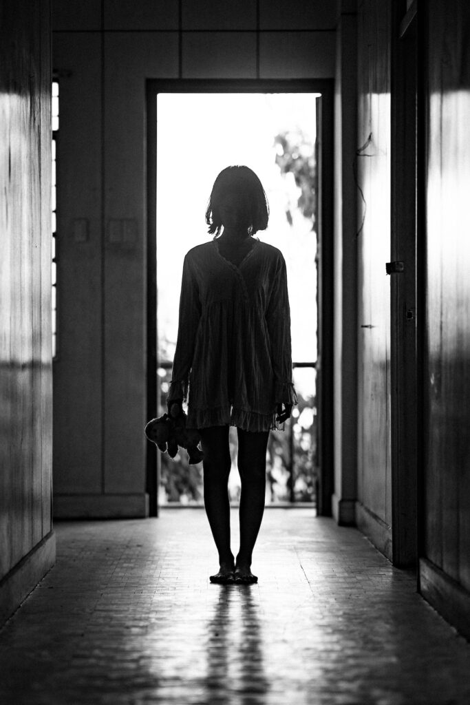A creepy black and white shot of a silhouette of a girl against a bright background.