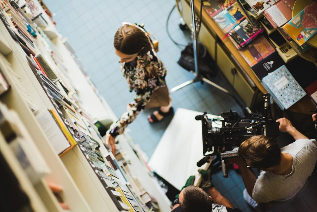 A movie scene of a woman in a book store as two men film her.