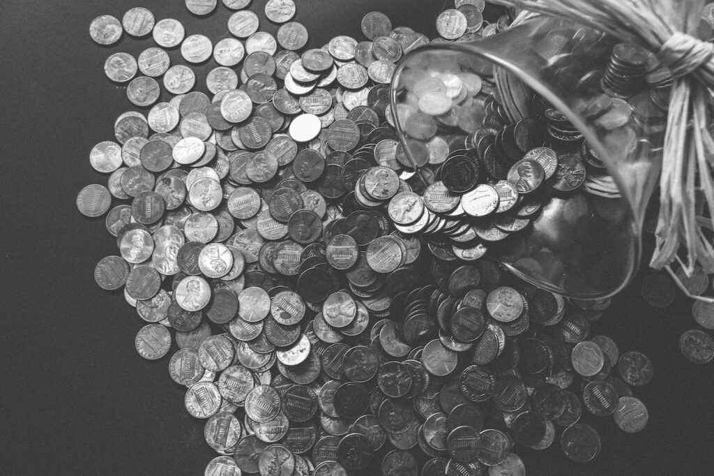 A pile of coins spilling out from a glass bowl and onto a table.