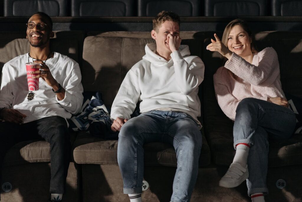 Three viewers in a theatre laughing at a movie.