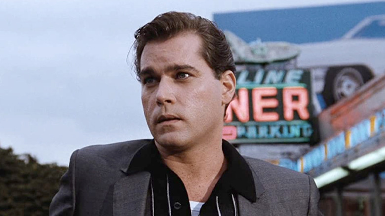 A character from the movie "Goodfellas" in front of a neon sign.