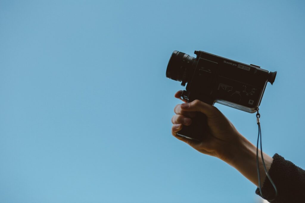 A person holding up a small camcorder against a blue background.